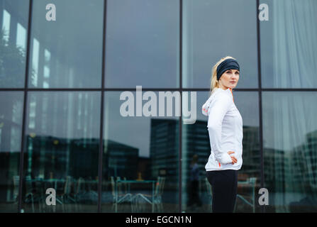 Porträt der selbstbewusste junge Frau stehend mit den Händen auf den Hüften, Blick in die Kamera. Fitness-Modell im Freien. Stockfoto