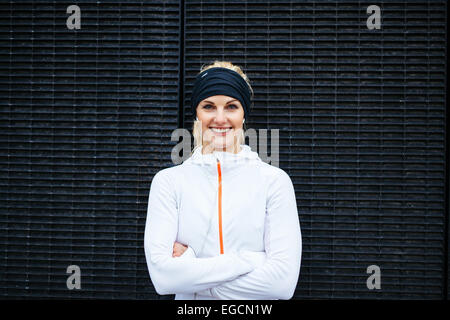 Porträt der glückliche junge Frau in Sportkleidung, Blick auf die Kamera zu Lächeln. Fitness Frauen gegen dunkle Wand. Stockfoto