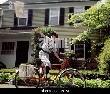 1960ER JAHRE JUNGE IM BASEBALL EINHEITLICHE REITEN FAHRRAD LIEFERN ZEITUNGEN Stockfoto