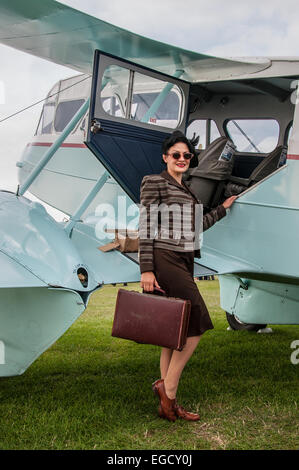 Ein Mädchen in Kostümen neben einem Flugzeug am Goodwood Revival 2014 posieren. Frauen in klassischen Vintage Zeitraum Kleid in der Luftfahrt. Mode Stockfoto