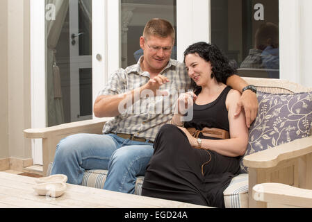 Wenige junge Erwachsene sitzen draußen auf der Veranda ihres Hauses auf einer bequemen Couch miteinander kommunizieren. Stockfoto