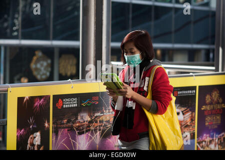 Eine Frau mit einem gelben Beutel trägt eine grüne Gesichtsmaske. Sie geht und liest ihr iPad/Tablet zur gleichen Zeit. Stockfoto