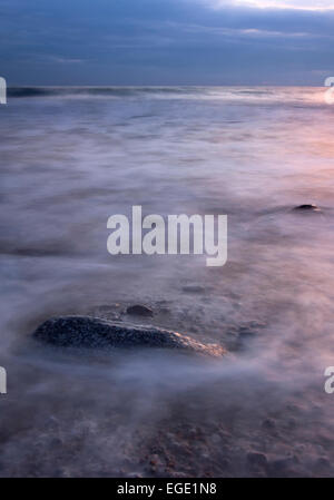 Meerwasser wäscht über einem Felsblock bei Sonnenuntergang. Cornwall, UK. Stockfoto