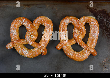 Zwei große Sauerteig Brezeln auf ein Backblech legen. Die gesalzene Snacks sind Seite an Seite im Querformat. Stockfoto