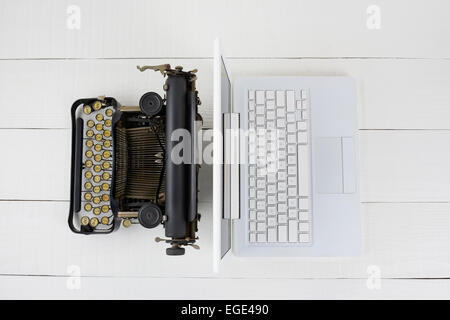 Overhead Schuss und alte altmodische Schreibmaschine Rücken an Rücken mit einem modernen Laptop-Computer auf einem weißen Holz Schreibtisch. Stockfoto