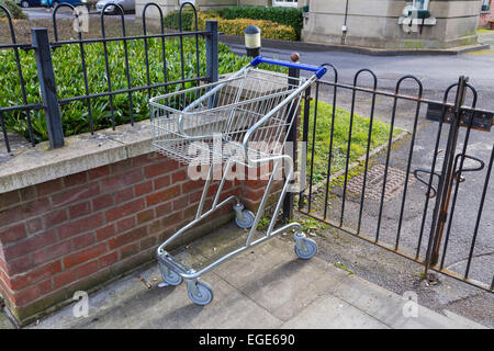 Ein verlassener Einkaufswagen links auf eine Straße in Salisbury gegen eine niedrige Mauer und Geländer. Stockfoto