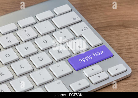 Wenden Sie nun auf einen großen blauen Knopf einer modernen Tastatur auf einem hölzernen Desktop geschrieben Stockfoto