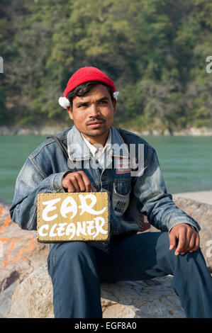 Ein lokaler Ohr Cleaner sitzt an der Seite des Flusses Ganges, in der Hoffnung, Kunden zu gewinnen und bietet kostenlose Bewertungen in Rishikesh, Indien Stockfoto