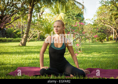 Junge Frau, die Yoga Übungen in den üppigen tropischen Garten Stockfoto