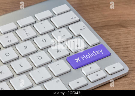 Urlaub und Flugzeug-Symbol auf einen großen blauen Knopf einer modernen Tastatur auf einem hölzernen desktop Stockfoto