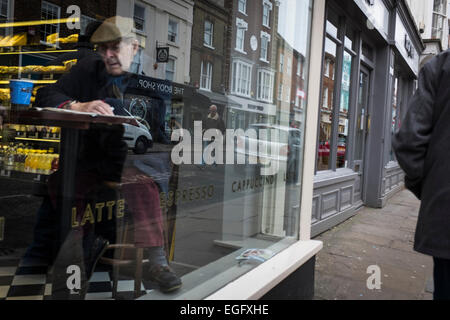 Älterer Mann in einem Café Ablesen des Papiers durch das Fenster mit der Reflexion von der Straße und Passanten. Stockfoto