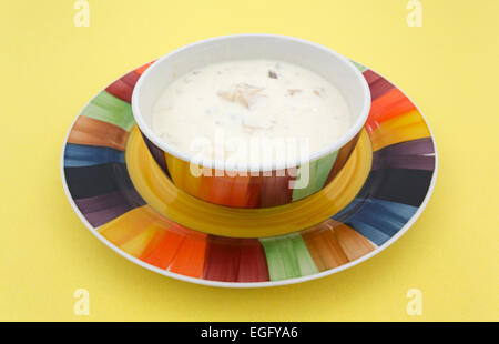 Eine Schüssel mit Muschelsuppe mit Kartoffeln in eine bunte Schüssel auf einem Teller auf eine gelbe Tischplatte. Stockfoto