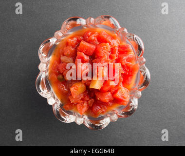 Draufsicht der gewürfelte Tomaten in Tomatensaft mit Jalapeño Paprika in eine Glasschüssel auf eine dunkle Tischplatte hinzugefügt Stockfoto