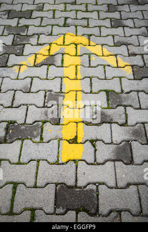 Gelber Pfeil auf graue Kopfsteinpflaster, Richtung Straßenschild Stockfoto