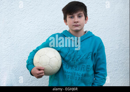 Junge, 10 Jahre, hält einen Fußball unter dem Arm, steht man vor einer weißen Wand, Baden-Württemberg, Deutschland Stockfoto