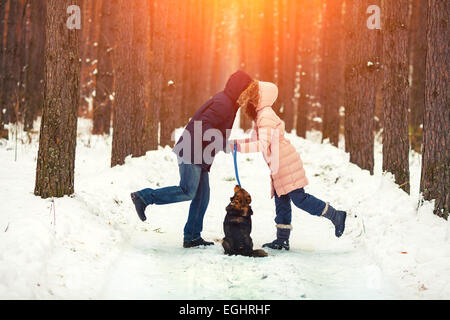 Junges Paar in Liebe mit Hund im verschneiten Wald spazieren und küssen Stockfoto