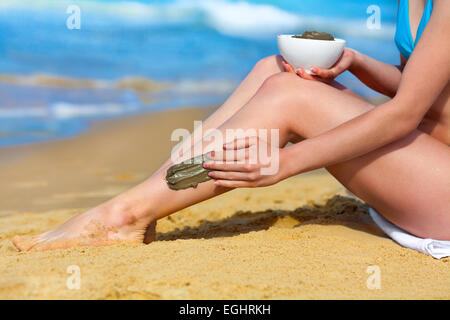 Junge schlanke Frau Verschmieren Schlamm-Maske auf den Körper am Strand Stockfoto