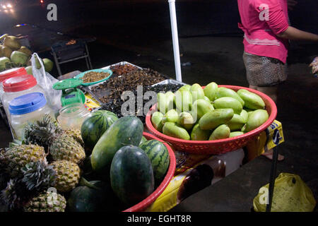 Wassermelonen und Ananas zusammen mit sortierten Insekten stehen zum Verkauf als Straße Nahrung in der Nacht in Kampong Cham, Kambodscha. Stockfoto