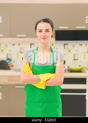 jungen kaukasischen lächelnden Frau mit Schürze und Gummihandschuhe, stehend in der Küche Stockfoto