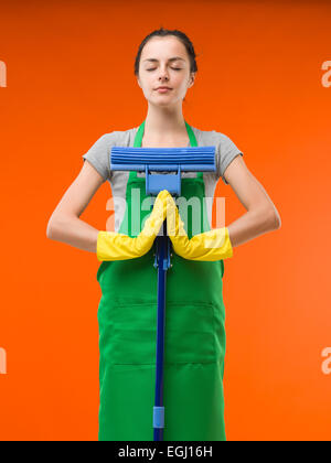 glücklich Putzfrau auf orangem Hintergrund mit gedrückter Mop, meditieren Stockfoto