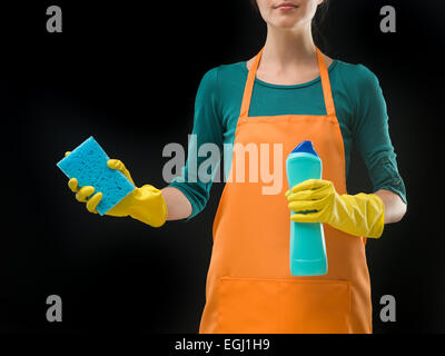 Hausfrau, halten Sie die Flasche mit der Reinigung Reinigungsmittel und Schwamm auf schwarzem Hintergrund Stockfoto