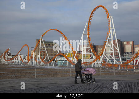 Frau schiebt einen Kinderwagen Zwillinge entlang der Promenade in Coney Island mit Thunderbolt Achterbahn in den Hintergrund-dur Stockfoto