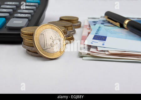 Euro (EUR)-Münzen, Rechnungen, einen Taschenrechner und einen Stift mit einer 1 Euro Münze vor. Stockfoto