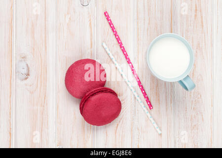 Bunte Macarons und Tasse Milch auf weißer Holztisch mit Textfreiraum Stockfoto
