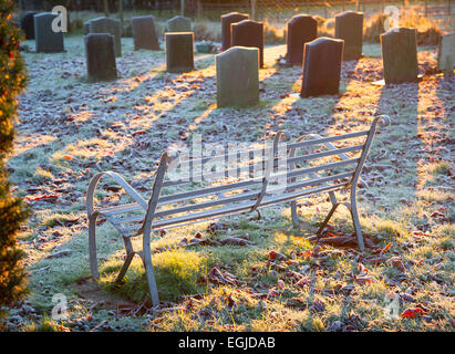 Frost bedeckt Metallsitz und Grabsteine in einem Dorf-Friedhof in Herefordshire, England, am frühen Morgen des gefrorenen Wintermorgen. Stockfoto