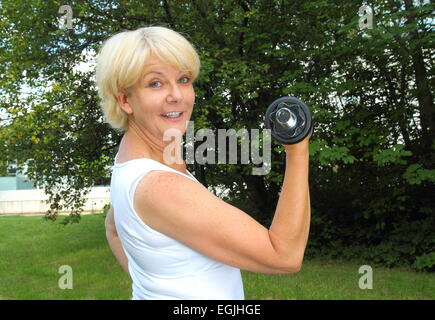 Eine ältere Frau, die dabei im freien Training in einem Park mit Hantel Stockfoto