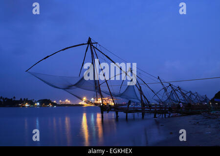 Chinesische Fischernetze in Fort Kochi, Kerala, Südindien am Abend blaue Stunde mit Vallarpadom Container Terminal als Kulisse. Stockfoto