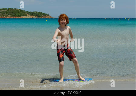 Junge mit seinem Surfbrett, Strand Board oder Skimboarden Surfen, am Strand, Bucht von Rondinara, Südostküste, Korsika, Frankreich Stockfoto