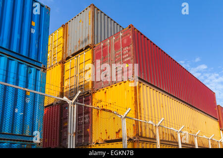 Bunte industrielle Luftfracht-Container gestapelt hinter Metall-Zaun mit Stacheldraht Stockfoto