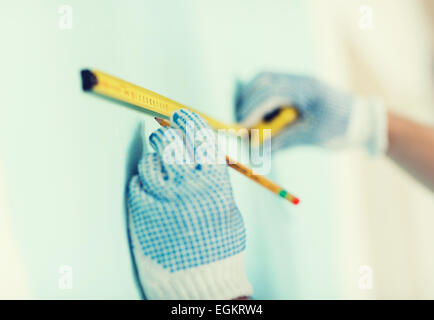 Nahaufnahme des Mannes in Handschuhen messen Wand mit Klebeband Stockfoto