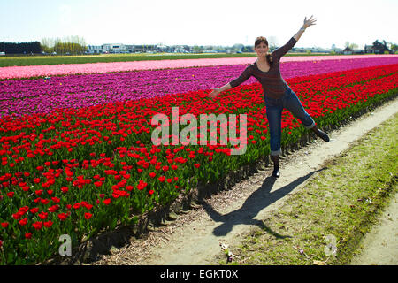 schöne junge Frau tanzen Spaß auf der Wiese mit roten und gelben Blumen Tulpen im Freien hellen Tag Stockfoto