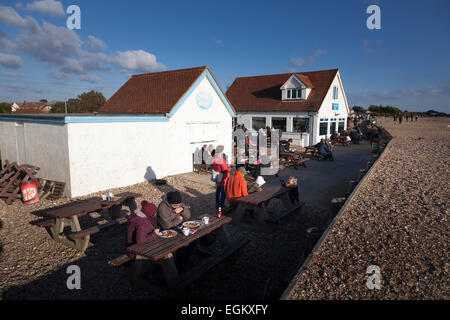 Kunden sitzen vor dem Bluebird-Strand-Café am Ferring Strand in der Wintersonne Stockfoto