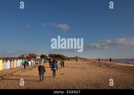 Menschen zu Fuß entlang Kiesstrand bei tief stehender Sonne vorbei Strandhütten Stockfoto