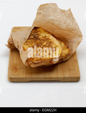 Geröstete Gourmet-Schinken und Käse-Sandwich in braune Papiertüte auf hölzernen Brot-Brett Stockfoto