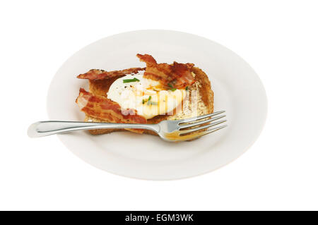 Pochiertes Ei mit Schnittlauch und Speck auf Vollkorn Toast mit einer Gabel auf einem Teller isoliert gegen weiß Stockfoto