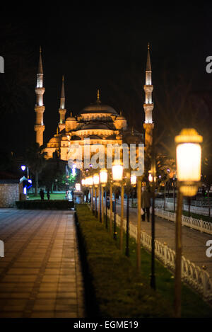 Sultan-Ahmed-Moschee Blaue Moschee bei Nacht Istanbul Türkei | ISTANBUL — Ein langer Weg von beleuchteten Laternenpfählen führt zur Sultan-Ahmed-Moschee, deren stufenartige Kuppeln und sechs Minarette gegen den Nachthimmel über dem Sultanahmet-Platz beleuchtet sind. Die 1616 unter Sultan Ahmed I. fertiggestellte Moschee wird wegen ihrer inneren Kachelarbeit allgemein als Blaue Moschee bezeichnet. Fußgänger gehen auf der Promenade, einst das Gelände des byzantinischen Hippodroms. Stockfoto