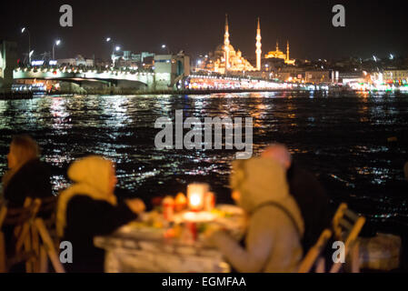 Blick auf die neue Moschee und die Galatebrücke vom Goldenen Horn Istanbul // ISTANBUL, Türkei – die Gäste genießen Mahlzeiten in Restaurants im Freien am Goldenen Horn in Karakoy, Istanbul. Die historische neue Moschee (Yeni Cami), die 1665 fertiggestellt wurde, und die Galata-Brücke bilden eine dramatische Kulisse. Diese beliebten Restaurants am Wasser bieten frische Meeresfrüchte und traditionelle türkische Küche mit Blick auf die historische Skyline Istanbuls. Stockfoto