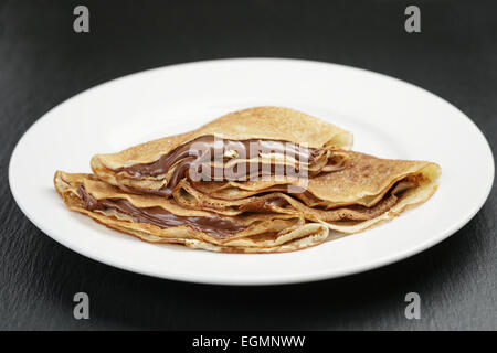 dünne Crepes oder Blinis mit Schokoladencreme auf Platte Stockfoto