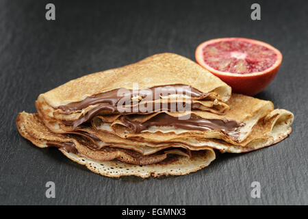Crepes oder Blinis mit Schokoladencreme und Orange auf Schiefer Stockfoto