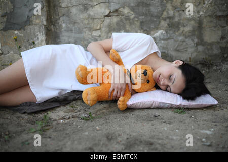 Schlafmütze Mädchen schläft auf der Straße mit Teddybär Stockfoto