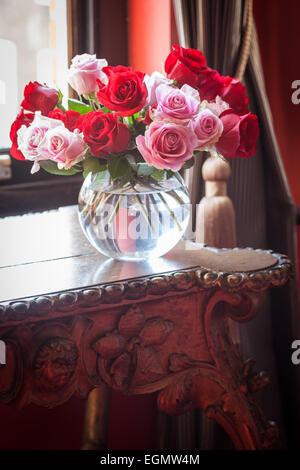 Vase mit Rosen auf antiken Tisch im Fenster Stockfoto