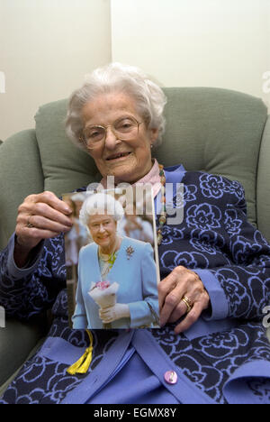 Frau feiert ihren 100. Geburtstag und hält die traditionelle Karte erhalten von ihrer Majestät der Königin beim Erreichen dieses... Stockfoto