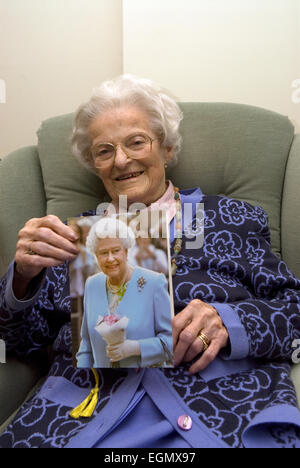 Frau feiert ihren 100. Geburtstag und hält die traditionelle Karte erhalten von ihrer Majestät der Königin beim Erreichen dieses... Stockfoto