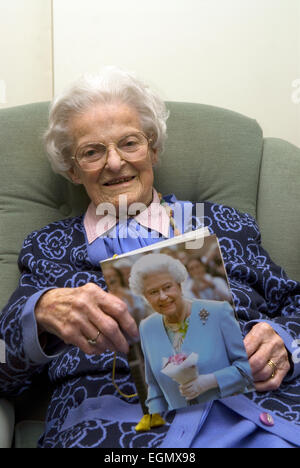 Frau feiert ihren 100. Geburtstag und hält die traditionelle Karte erhalten von ihrer Majestät der Königin beim Erreichen dieses... Stockfoto