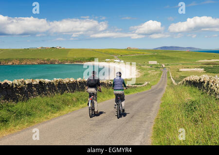 Junger Mann und Frau Radfahren entlang einer ruhigen Straße auf South Ronaldsay, Orkney Inseln, Schottland. Stockfoto