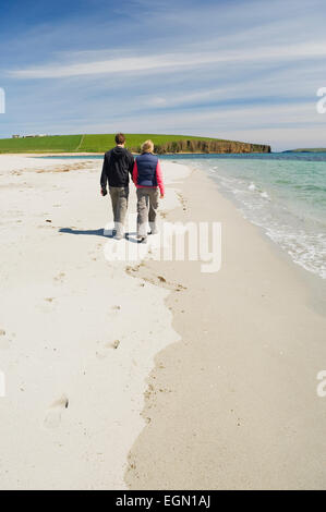 Junge Frau und Mann zu Fuß an einem schönen Sandstrand im Sommersonnenschein, Dingieshowe, Deerness, Orkney Inseln, Schottland. Stockfoto
